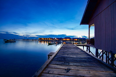 Pier and houses at jetty on sea during sunset