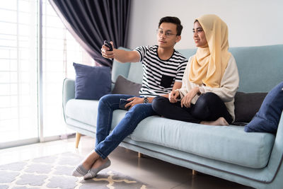 Couple watching tv while sitting on sofa at home