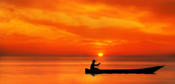 Silhouette man in sea against orange sky