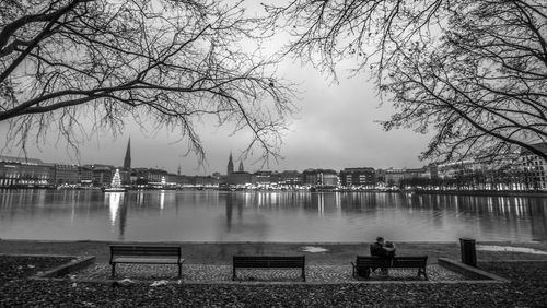 People sitting on bench by river against sky