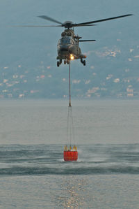 Helicopter carrying water in container over sea