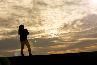 Silhouette woman standing on field against sky during sunset