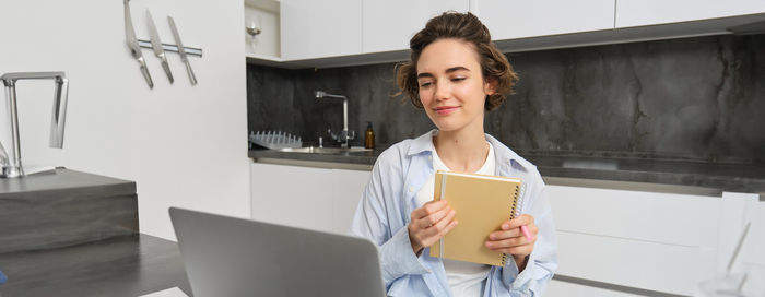 Portrait of young woman using digital tablet while standing against wall