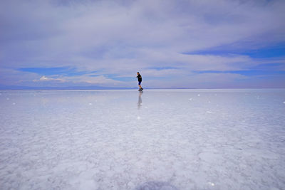 Full length of man standing on salt flat against cloudy sky