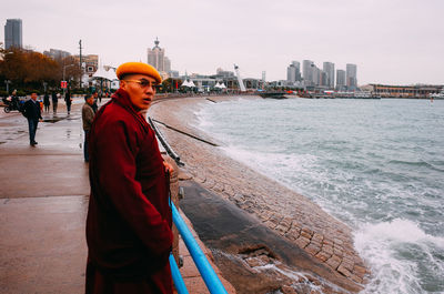 Side view of man standing in city by sea against sky