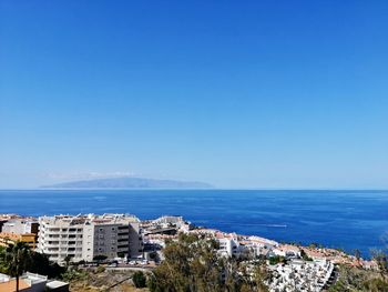 Scenic view of sea by buildings against clear blue sky