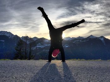 Man doing handstand on road by snowcapped mountain against sky