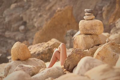 Low section of woman relaxing at beach by rock formations