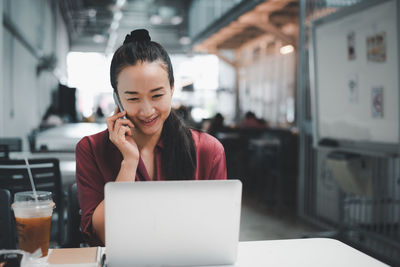 Young woman looking away while sitting on laptop