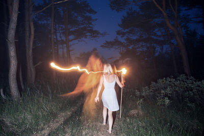 Rear view of woman walking with flaming torch in forest at night