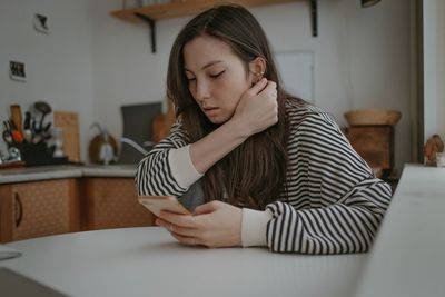 Young woman using mobile phone while sitting on bed at home