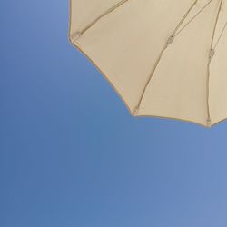 Low angle view of parasol against clear blue sky