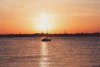 Silhouette sailboat sailing on sea against orange sky