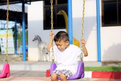 Cute boy looking down sitting on swing at playground