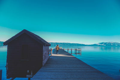 Rear view of man walking on pier against lake and sky