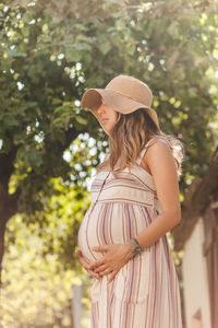 Woman wearing hat standing against trees