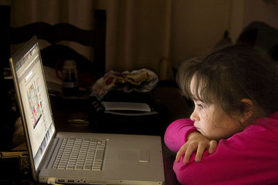 Cute girl looking at laptop while sitting on table at home