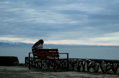 Lifeguard sitting on bench by sea against sky