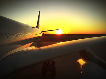 Close-up of airplane wing on runway against sky during sunset