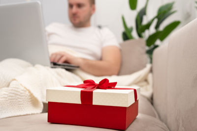 Man using laptop while sitting on sofa at home. focus at gift box. holiday online shopping 