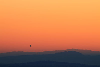 Silhouette hot air balloon against orange sky