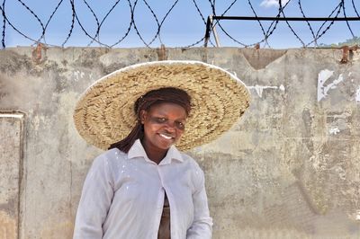Portrait of smiling woman wearing straw hat against wall