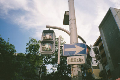 Low angle view of arrow symbol on street light pole by building against sky