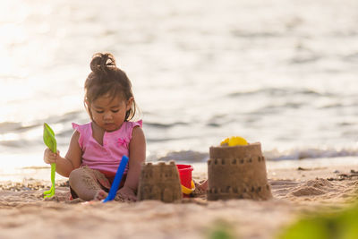 Cute girl making sandcastle sitting on beach