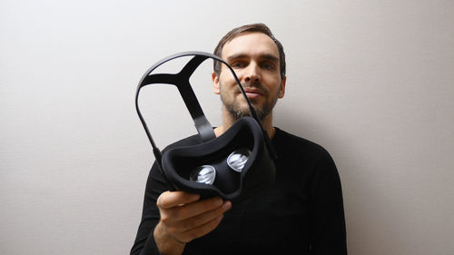 Portrait of young man holding remote control against wall