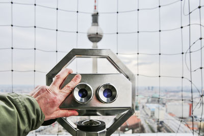 Close-up of man holding coin-operated binoculars against fernsehturm