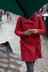 Rear view of woman with red umbrella standing on footpath