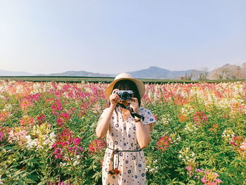 Woman photographing with pink flowers against sky