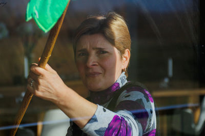 Close-up portrait of woman holding stick seen through window