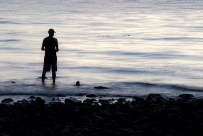 Rear view of silhouette man standing at beach during sunset