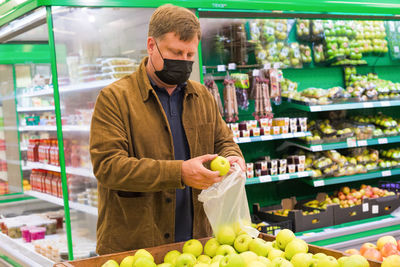 Adult man in a black protective mask in shopping center chooses fruit.