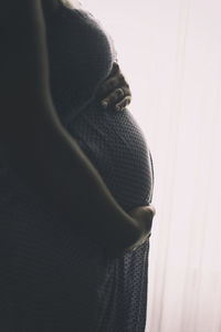 Midsection of pregnant woman standing by curtain