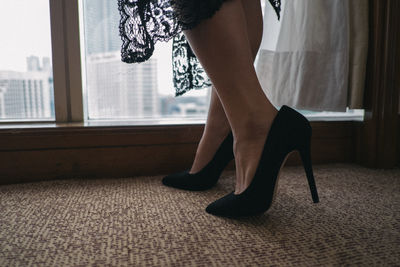 Low section of woman wearing black high heels by window at home