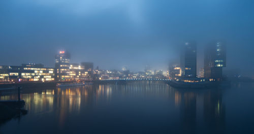 Illuminated buildings by river against sky in city at night