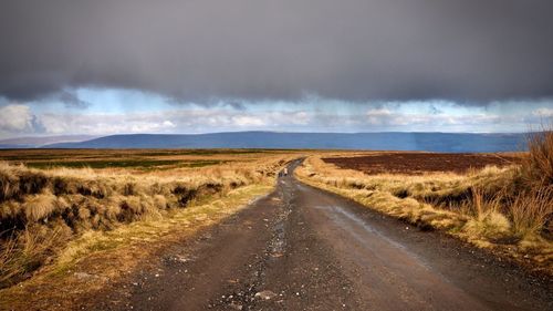 Road passing through field against cloudy sky