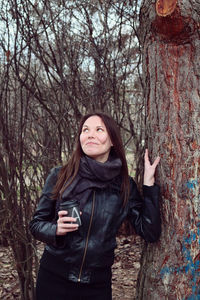 Smiling young woman standing by tree trunk in forest