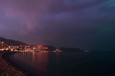 Illuminated city by sea against sky at night