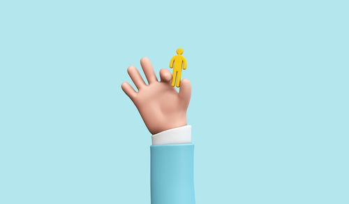 Close-up of hand holding yellow toy against blue background