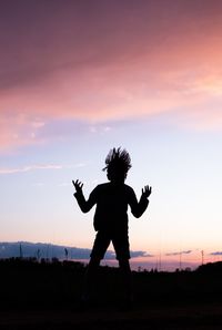 Silhouette of kif jumping on field against sky during sunset