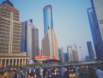 Low angle view of crowd in city against clear sky