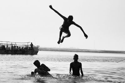 Men jumping in sea against clear sky