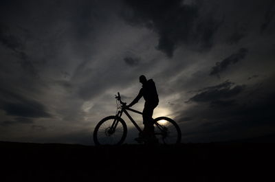 Silhouette man with bicycle against sky at sunset