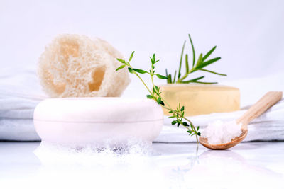 Close-up of soaps with herbs on table against white background