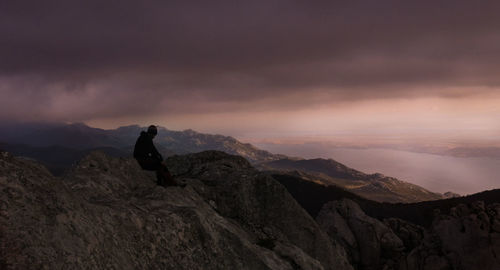 Silhouette woman sitting on mountain against sky during sunset