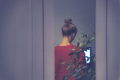 Rear view of woman standing against wall at home