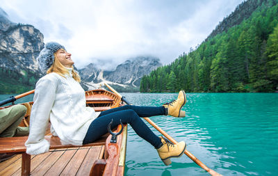 Woman sitting by lake against mountains